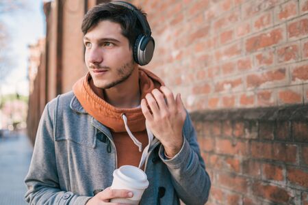 Portrait of young man with earphones and a cup of coffee against brick wall. Outdoors. Urban concept.の写真素材
