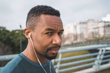 Portrait of an athletic man listening to music with earphones while resting for exercise outdoors....