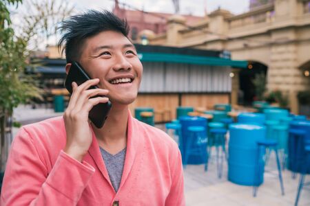 Portrait of young Asian man talking on the phone outdoors. Communication concept.