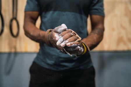 Portrait of fitness young man rubbing hands with chalk magnesium powder, preparing for workout in...