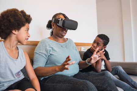 Portrait of African American grandmother and grandchildren playing together with VR glasses at home....
