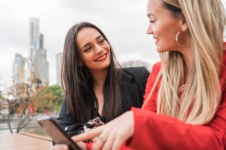 Portrait of two young friends using their mobile phone while sitting at coffee shop. Lifestyle and...