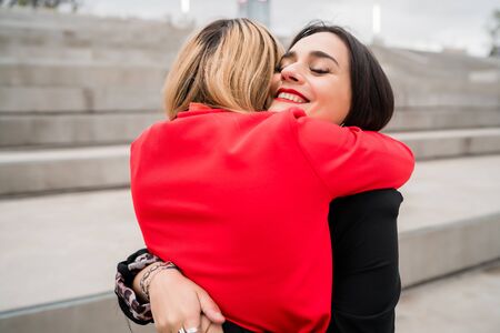 Portrait of two young friends hugging each other outdoors at the street. Lifestyle and friendship concept.の写真素材
