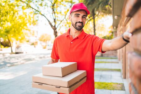Portrait of a delivery man with cardboard pizza box ringing house doorbell. Delivery and shipping service concept.の写真素材