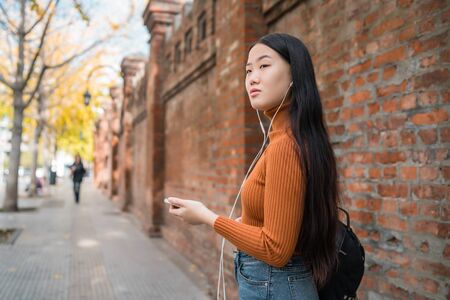 Portrait of young Asian woman listening to music with earphones in the street. Outdoors.の写真素材