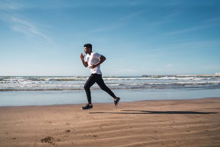 Portrait of an athletic man running at the beach. Sport, fitness and healthy lifestyle.