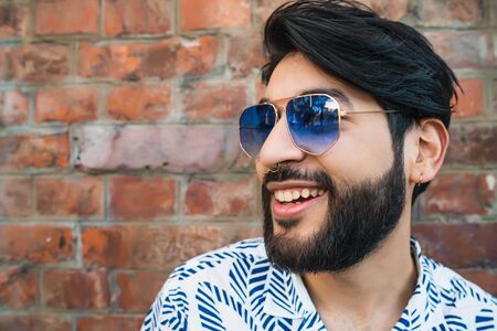Portrait of young handsome man wearing summer clothes and sunglasses against brick wall. Urban concept.の写真素材