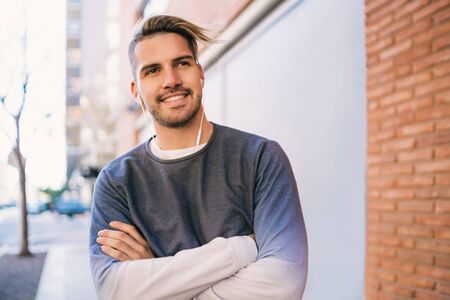 Portrait of young handsome man listening to music with earphones outdoors in the street. Urban...