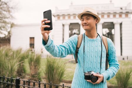 Portrait of young asian tourist taking a selfie with mobile phone outdoors in the street. Travel and technology concept.の写真素材
