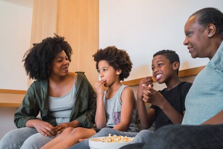 Portrait of African American grandmother, mother and children watching a movie and eating popcorn...