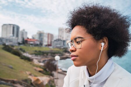 Portrait of young latin woman enjoying free time and listening to music with earphones outdoors. Music, lifestyle.の写真素材