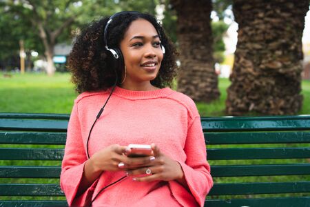 Portrait of young Afro american woman listening to music with headphones and mobile phone in the...