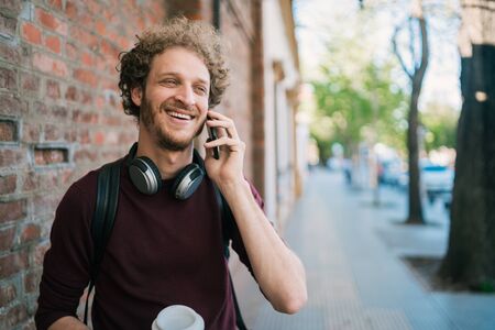 Portrait of young man talking on the phone while walking outdoors in the street. Communication and urban concept.の写真素材