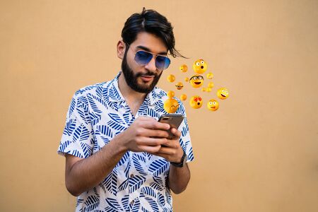 Young man using smartphone sending emojis. Outdoors. Social media concept.の写真素材