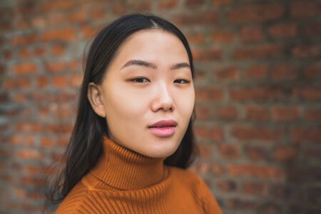 Close up of young beautiful Asian woman looking confident and standing against brick wall background.の写真素材