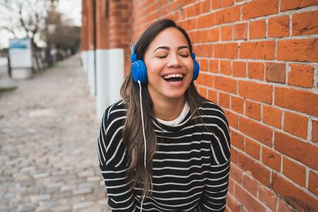Portrait of young beautiful woman smiling and listening to music with blue headphones in the street. Outdoors.の写真素材