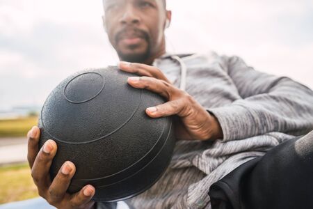 Portrait of an athletic man doing abdominal exercise with medicine ball in the park outdoors. Sport and healthy lifestyle.の写真素材
