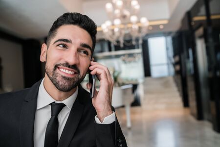 Portrait of young businessman talking on the phone at the hotel lobby. Business travel concept.の写真素材