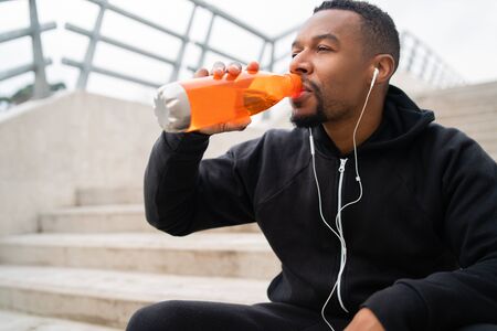 Portrait of an athletic man drinking something after training while sitting on concrete stairs. Sport and health lifestyle.の写真素材
