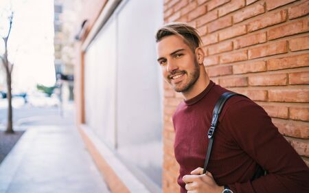 Portrait of young handsome man carrying a backpack and wearing casual clothes against the brick wall in the street. Urban concept.の写真素材