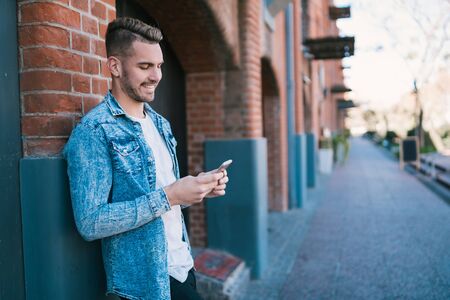 Portrait of young handsome man using his mobile phone outdoors in the street. Communication concept.の写真素材