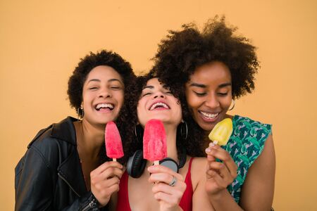 Portrait of multi-ethnic group of friends having fun and enjoying summertime while eating ice cream against yellow background.の写真素材