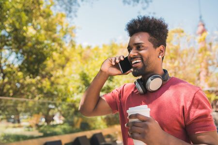 Portrait of young afro man talking on the phone while holding a cup of coffee outdoors....