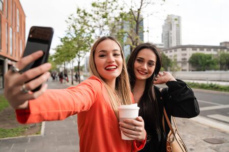 Portrait of two young friends taking a selfie with mobile phone at the street. Lifestyle and friendship concepts.の写真素材