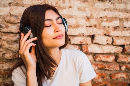 Portrait of young latin woman relax and listening to music with headphones against brick wall. Urban concept.の写真素材