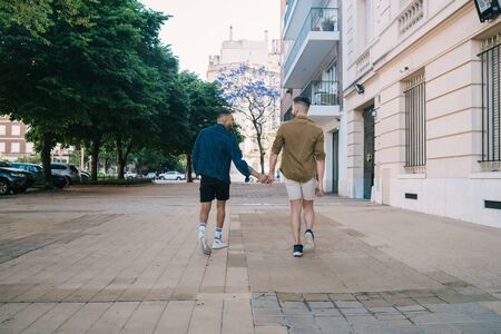 Portrait of happy gay couple spending time together and holding hands in the street. Lgbt and love...