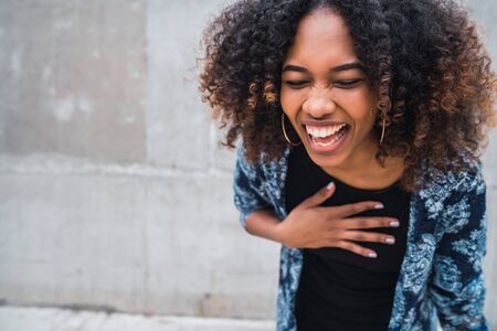 Portrait of beautiful young afro-american confident woman laughing against grey wall.