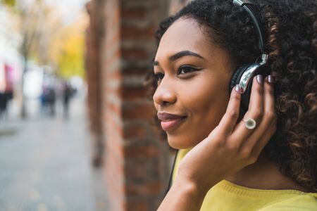 Portrait of young Afro american woman listening to music with headphones in the street. Outdoors.