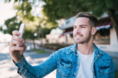 Portrait of attractive young man taking selfies with his mophile phone outdoors in the street....