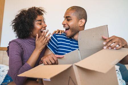 Portrait of happy young latin couple opening a package at home. Delivery, shipping and postal service concept. Buy online and stay at home. Covid-19 Quarantine.の写真素材