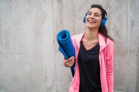 Portrait of an athletic woman holding a training mat while listening to music. Sport and lifestyle concept.の写真素材