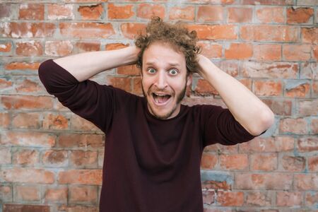 Portrait of young caucasian man with shocked gesture against the brick wall in the street. Urban concept.の写真素材