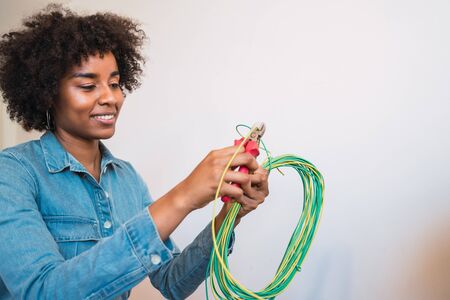 Portrait of young afro woman fixing electricity problem with cables at new home. Repair and renovation home concept.の写真素材
