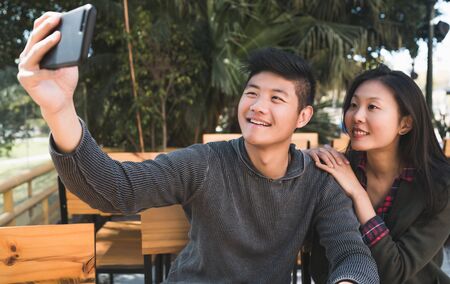 Portrait of a lovely asian couple having good time and taking a selfie with mobile phone in coffee shop.の写真素材