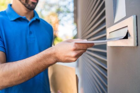 Close-up of a postman putting a letter in a house mailbox. Delivery postal service concept.