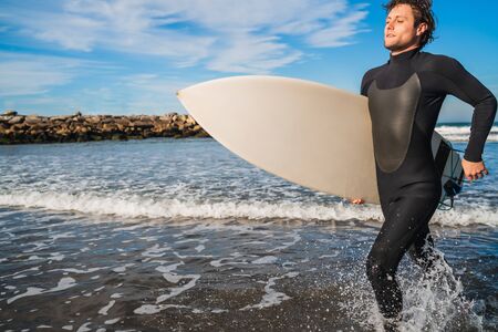 Portrait of young surfer leaving the water with surfboard under his arm. Sport and water sport concept.の写真素材