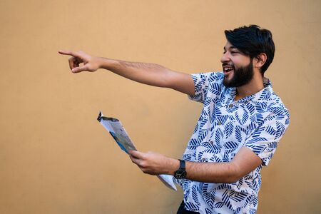 Portrait of young tourist man wearing summer clothes and holding a map looking for directions...
