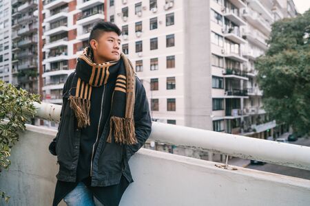 Portrait of young asian man looking confident and wearing winter clothes outdoors in the street....