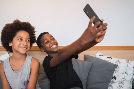 Portrait of two Afro American brothers taking a selfie with mobile phone at home. Lifestyle and...