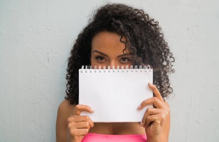 Portrait of young afro woman holding a blank paper. Showing or promoting something. Advertising concept.の写真素材