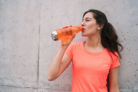 Portrait of an athletic woman drinking water after training against grey background. Sport and health lifestyle.の写真素材