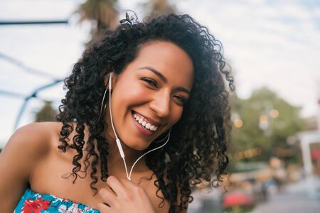 Portrait of young Afro american woman enjoying the day and listening to music with earphones in the street.の写真素材