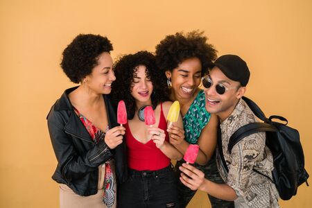 Portrait of multi-ethnic group of friends having fun and enjoying summertime while eating ice cream against yellow background.の写真素材