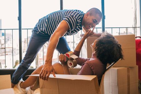 Portrait of happy latin couple having fun with cardboard boxes in new house at moving day. Real estate concept.の写真素材