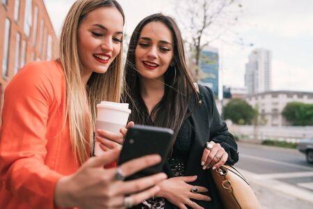 Portrait of two young friends taking a selfie with mobile phone at the street. Lifestyle and friendship concepts.の写真素材