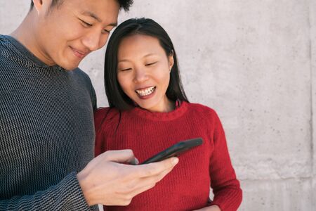 Portrait of lovely asian couple looking at the mobile phone while spending good time together. Love and technology concept.の写真素材